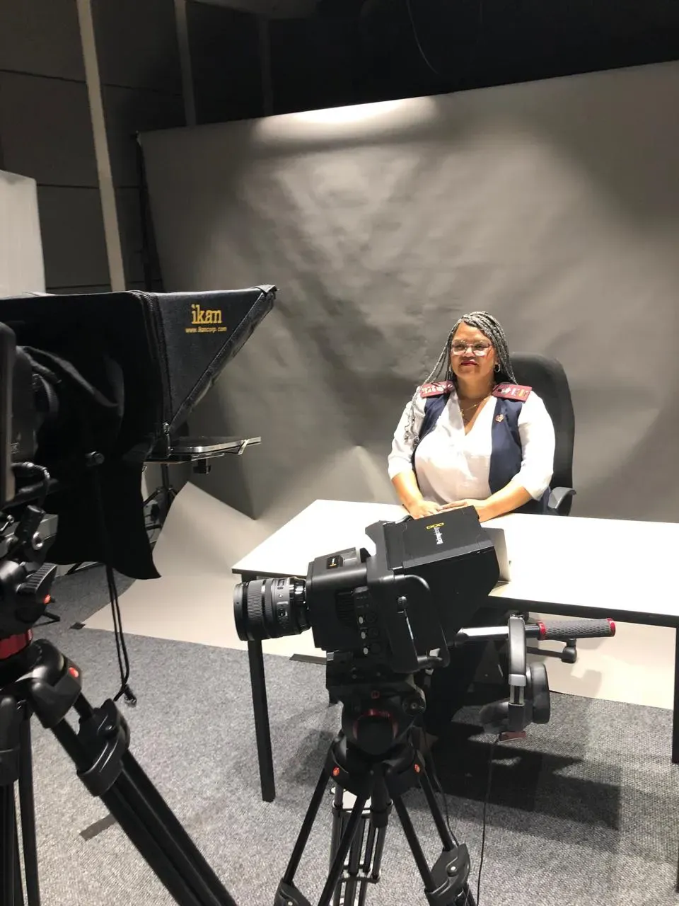 A speaker seated at a desk in a studio during a promotional video shoot